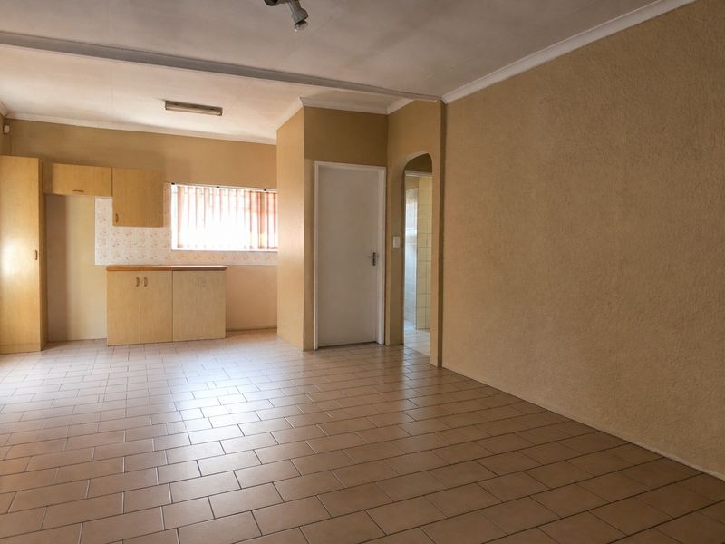 An open-plan living and kitchen area featuring tiled flooring, built-in cabinetry, and a neutral color palette, offering a blank canvas for renovation.