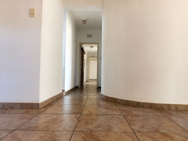A bright, empty hallway featuring tiled flooring and a distinctive curved wall design, leading through to additional interior spaces.