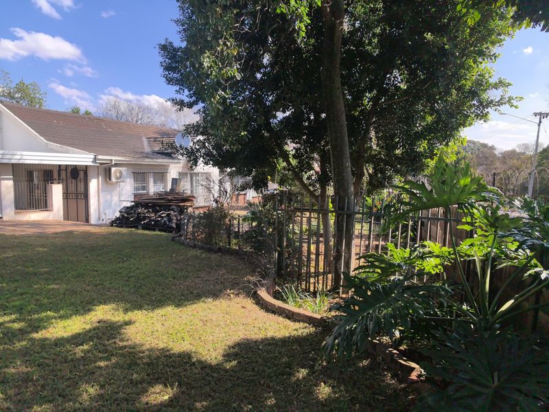 Rear view of the property featuring a lawn, mature trees, security fencing, and exterior access with security gates and an installed air conditioning unit.