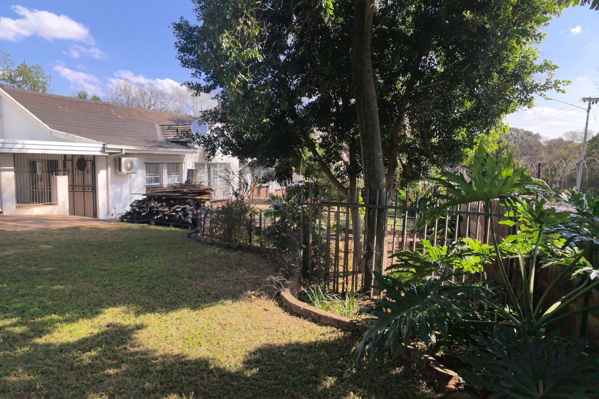 Rear view of the property featuring a lawn, mature trees, security fencing, and exterior access with security gates and an installed air conditioning unit.