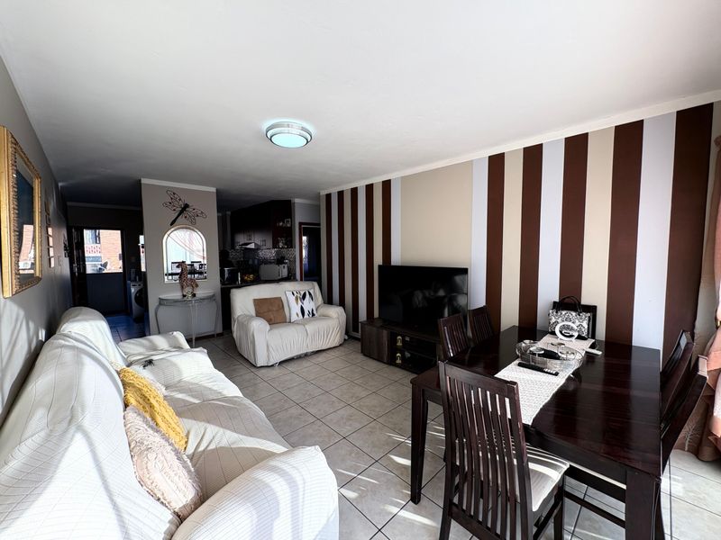 An open-plan living and dining area featuring tiled flooring, a decorative striped feature wall, and an archway leading to the kitchen.