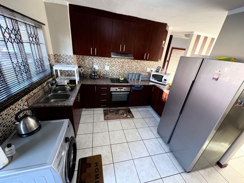 Functional kitchen featuring dark wood cabinetry, granite countertops, mosaic tile backsplash, and integrated appliances, including a built-in oven and hob.