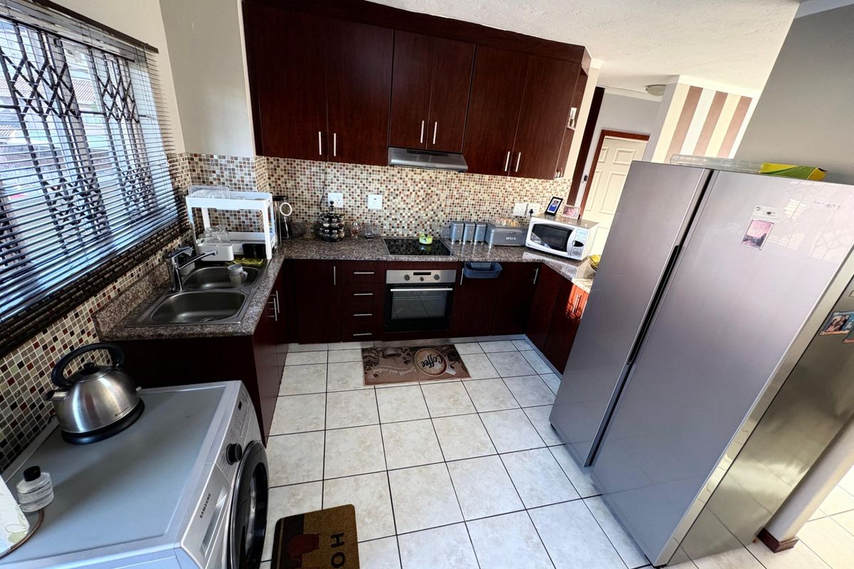 Functional kitchen featuring dark wood cabinetry, granite countertops, mosaic tile backsplash, and integrated appliances, including a built-in oven and hob.