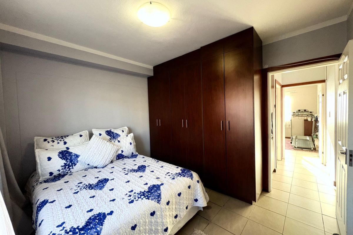 A bedroom featuring dark wood built-in cupboards and tiled flooring, with an adjacent hallway visible through the doorway.