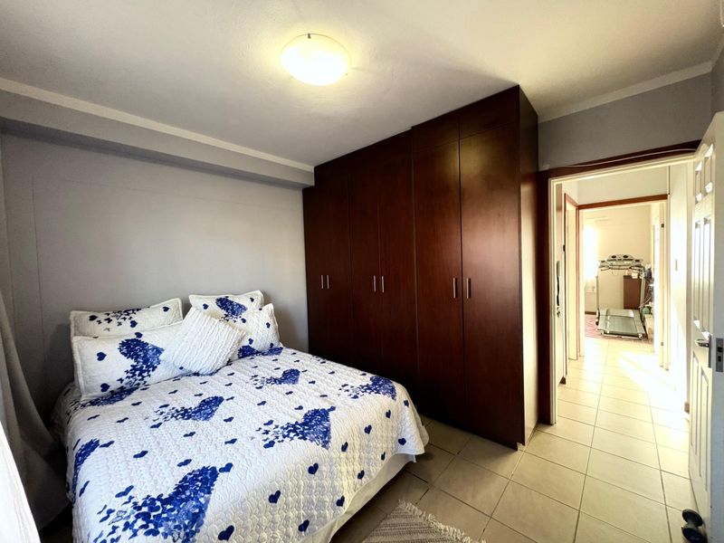 A bedroom featuring dark wood built-in cupboards and tiled flooring, with an adjacent hallway visible through the doorway.