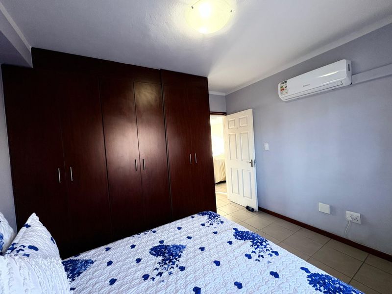A well-maintained bedroom featuring dark wood built-in cupboards, tiled flooring, and a wall-mounted air conditioning unit.