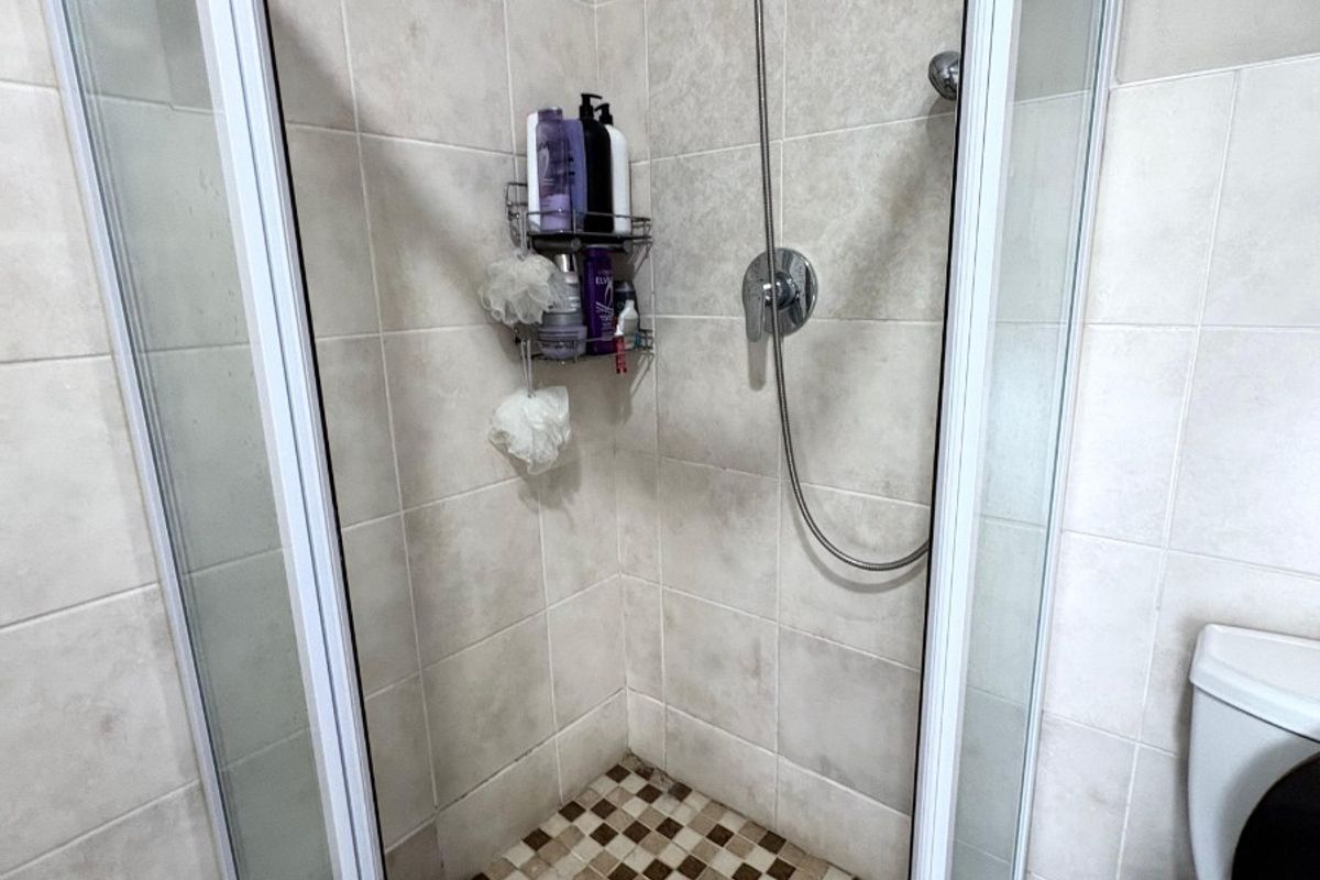 A functional bathroom featuring a corner shower enclosure with tiled walls and flooring, complemented by a standard toilet.