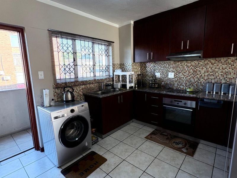 A functional kitchen featuring dark wood cabinetry, granite countertops, mosaic tile backsplash, and integrated appliances, with direct access to an outdoor balcony area.