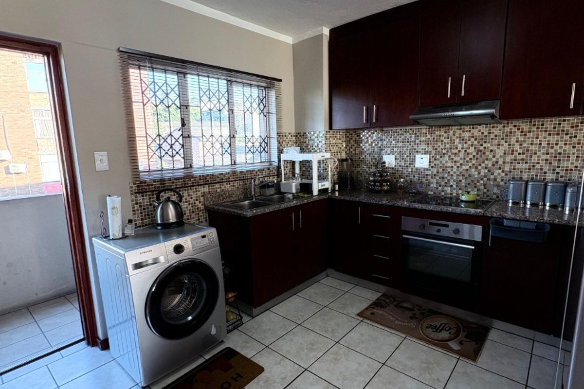 A functional kitchen featuring dark wood cabinetry, granite countertops, mosaic tile backsplash, and integrated appliances, with direct access to an outdoor balcony area.