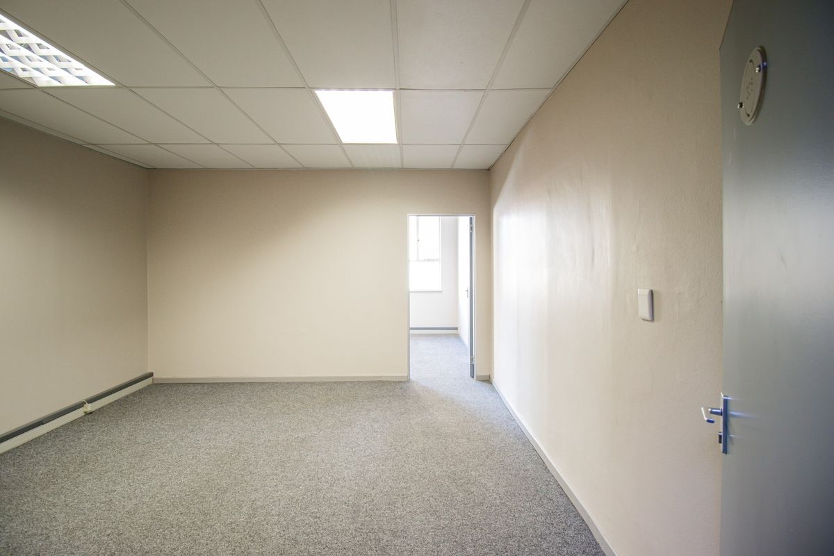 A vacant, neutral-toned office space featuring a suspended ceiling with recessed lighting and carpeted flooring, providing a clean and functional commercial work environment.