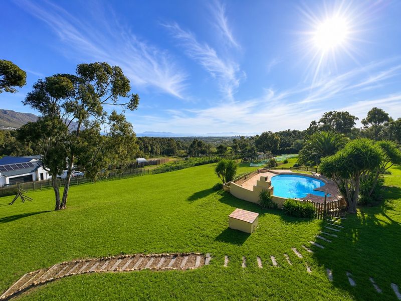 Expansive garden featuring a swimming pool with paved surround, stone pathway, and scenic landscape views under a clear blue sky.