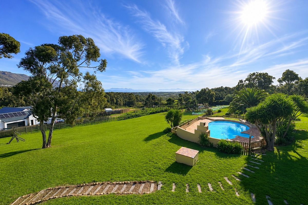 Expansive garden featuring a swimming pool with paved surround, stone pathway, and scenic landscape views under a clear blue sky.