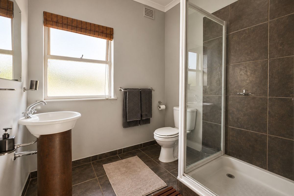 A modern bathroom featuring a pedestal washbasin, a toilet, and a glass-enclosed shower with dark tiled walls and flooring.