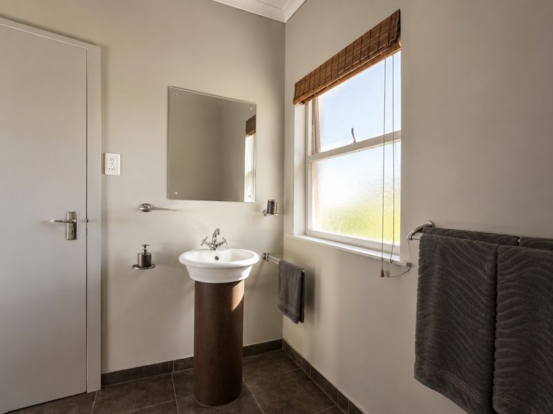 A clean and functional bathroom featuring a pedestal basin, chrome fixtures, tiled flooring, and a window providing natural light.
