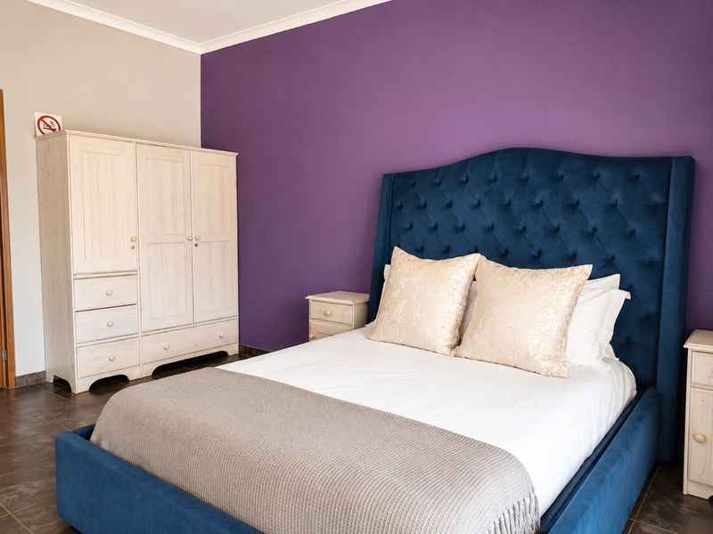 A well-maintained bedroom featuring dark tiled flooring, coving, and a bold purple accent wall.
