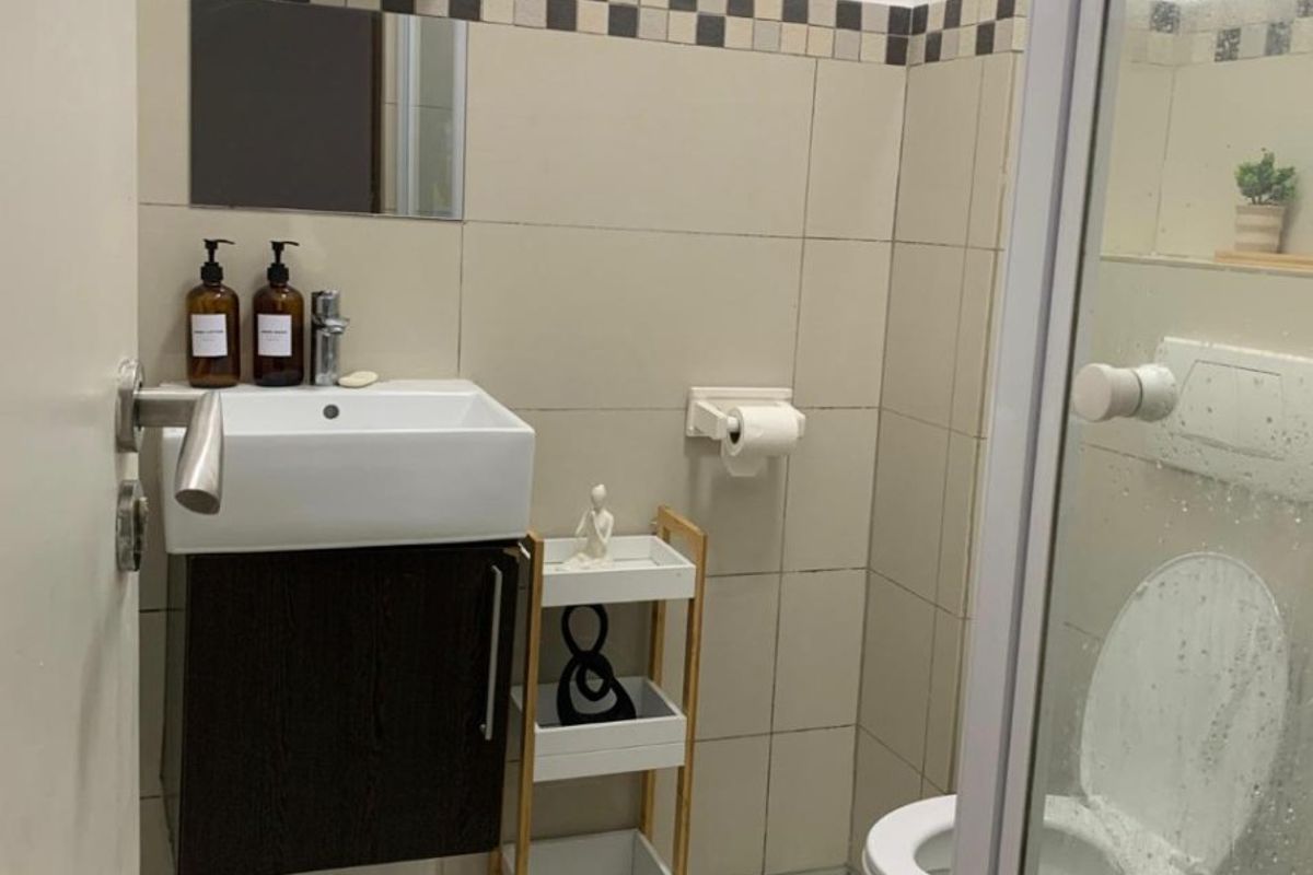 Compact bathroom featuring a wall-mounted vanity, ceramic basin, toilet, and a glass-enclosed shower with neutral wall tiling.