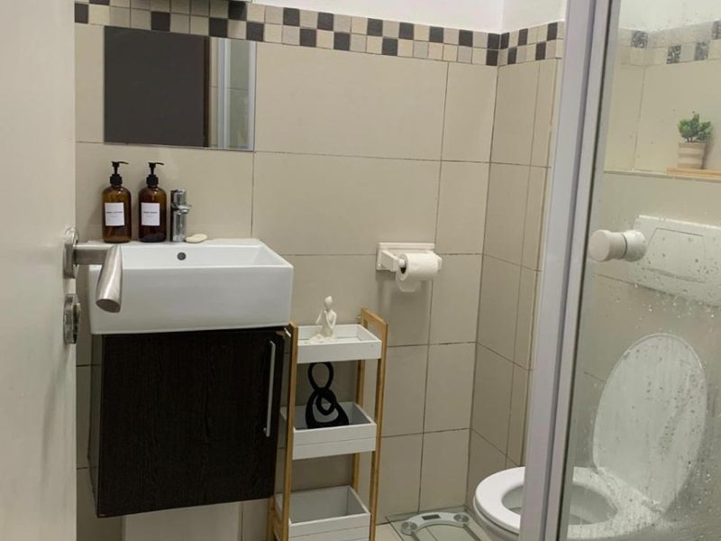 Compact bathroom featuring a wall-mounted vanity, ceramic basin, toilet, and a glass-enclosed shower with neutral wall tiling.