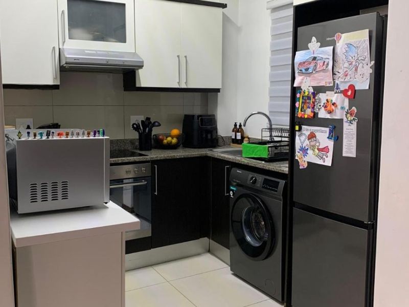 Compact modern kitchen featuring two-tone cabinetry, granite countertops, built-in oven, extractor fan, and integrated laundry facilities with tiled flooring.