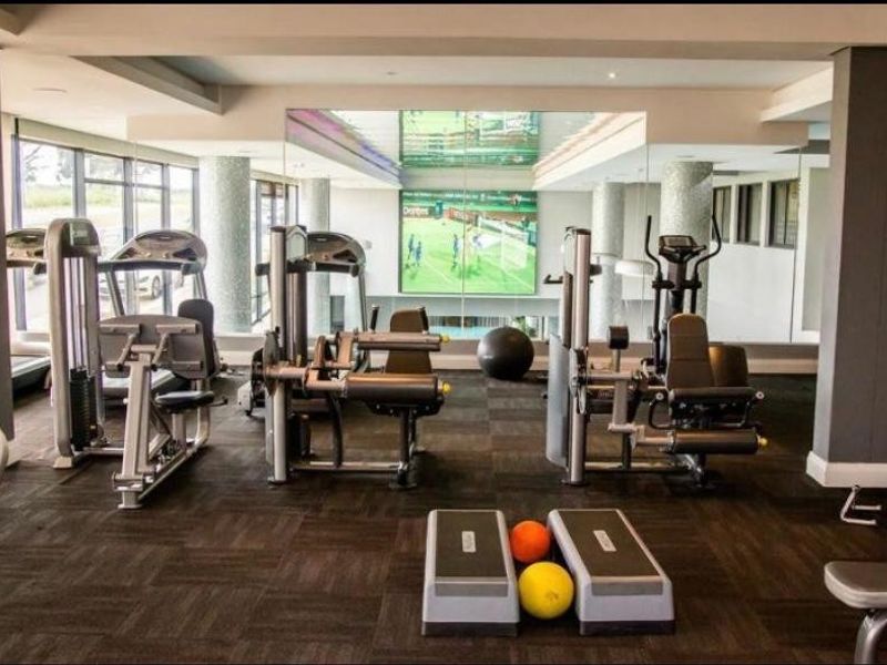 A well-equipped residential gym featuring mirrored walls, recessed lighting, and durable carpet flooring, providing a functional space for fitness and exercise.