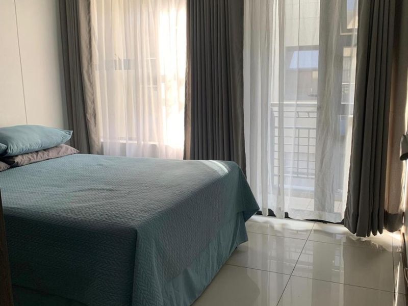 A bright bedroom featuring large sliding glass doors with curtains and polished tiled flooring, providing access to an outdoor balcony area.