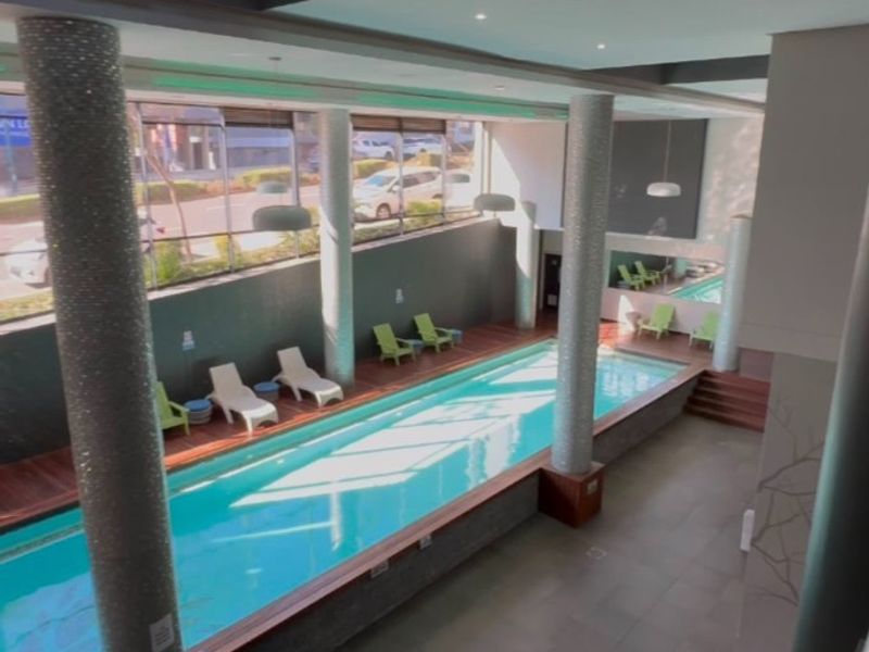 A modern indoor swimming pool area featuring large windows, decorative columns, and high-quality tiled finishes, providing a bright and well-maintained recreational space.