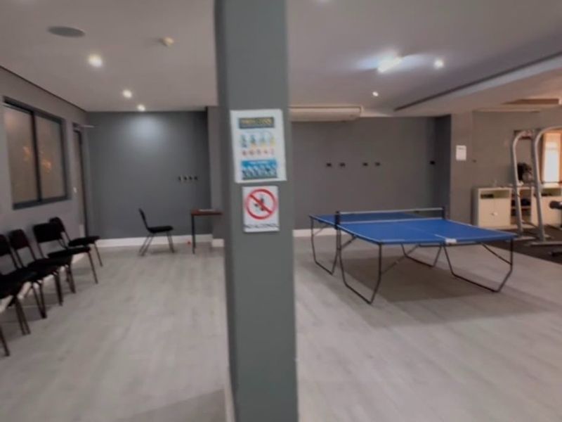 A spacious indoor recreational area featuring laminate flooring, recessed lighting, and an air conditioning unit, currently set up with table tennis equipment.