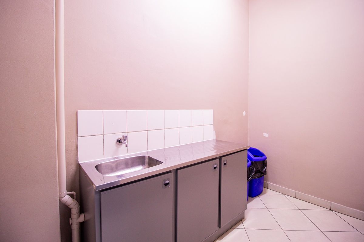 A functional utility or scullery area featuring a stainless steel sink, built-in cabinetry, tiled splashback, and tiled flooring.