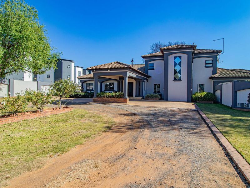 Front elevation of a lodge-style property featuring a covered entrance portico, paved driveway, and established garden with boundary walling.