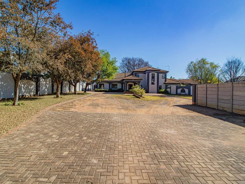 Spacious front exterior view featuring a large paved driveway, perimeter wall with electric fencing, and a well-maintained garden leading to the main house entrance.