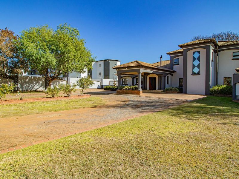 Front elevation of the property featuring a covered entrance portico, paved driveway, and established garden area.
