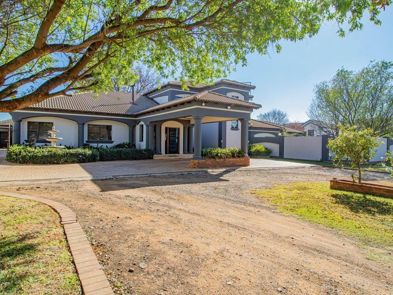 Front elevation of a spacious residence featuring a covered entrance portico, paved driveway, and established garden beds.