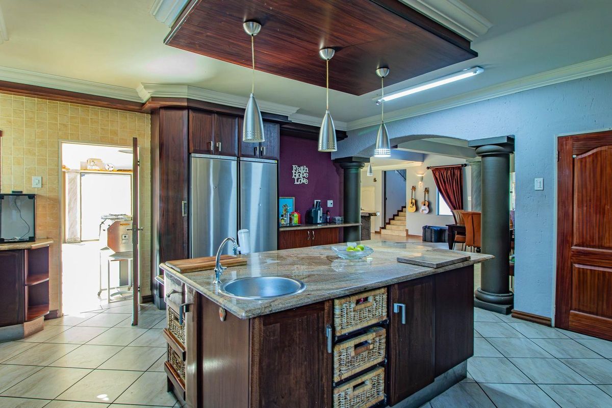 Spacious kitchen featuring a central island with granite countertops, dark wood cabinetry, pendant lighting, and a distinct drop ceiling feature.
