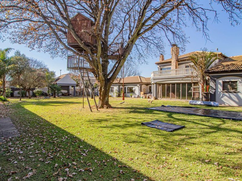 Spacious rear garden featuring a large lawn, mature tree with a treehouse, and a multi-level house exterior with a balcony and stone chimney.