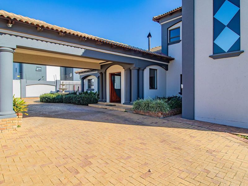 A well-maintained front entrance featuring a covered porte-cochere, brick paved driveway, and decorative columns leading to a solid wooden front door.