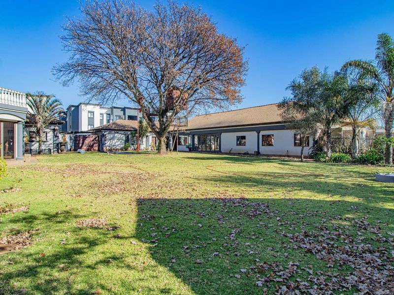 Spacious rear garden featuring a large lawn, mature trees, and a paved patio area adjacent to the main house structure.