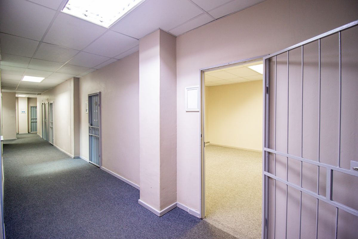 A commercial hallway featuring carpeted flooring, suspended ceilings with recessed lighting, and multiple access points secured by metal security gates.