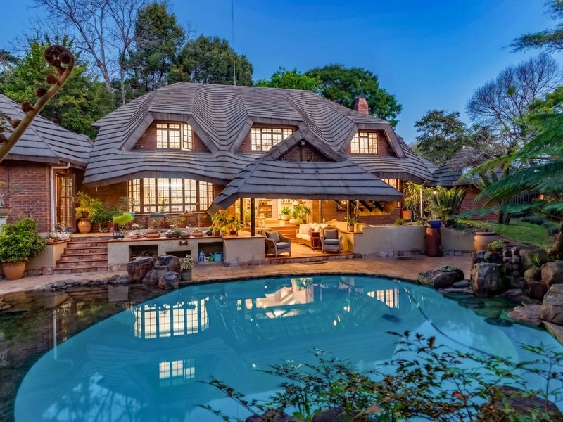 Rear view of a charming house featuring a unique tiled roof, a covered patio area, and a landscaped swimming pool.