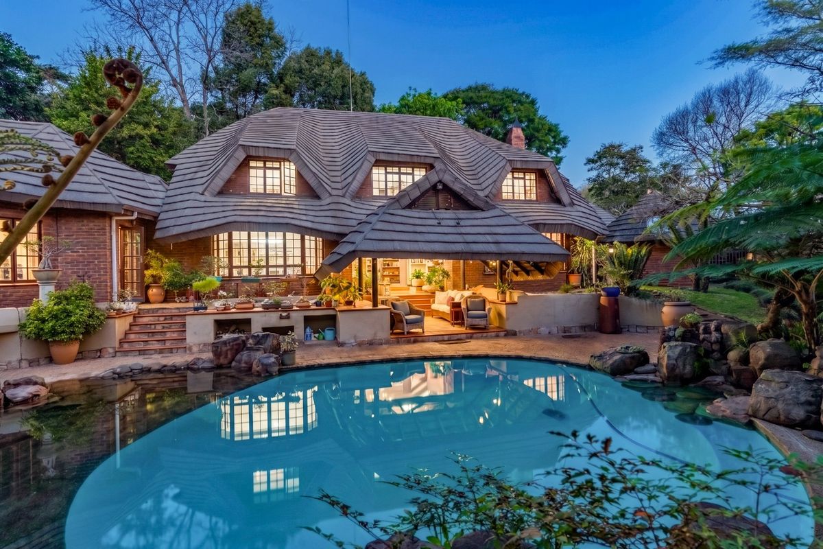 Rear view of a charming house featuring a unique tiled roof, a covered patio area, and a landscaped swimming pool.