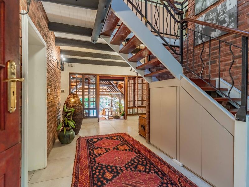 Welcoming entrance hall featuring exposed brick walls, timber ceiling beams, and a staircase with integrated under-stair storage cabinetry.