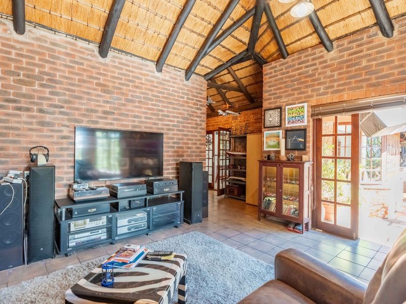 A rustic living room featuring exposed brick walls, a high thatched ceiling with timber rafters, tiled floors, and access to the outdoors via french doors.