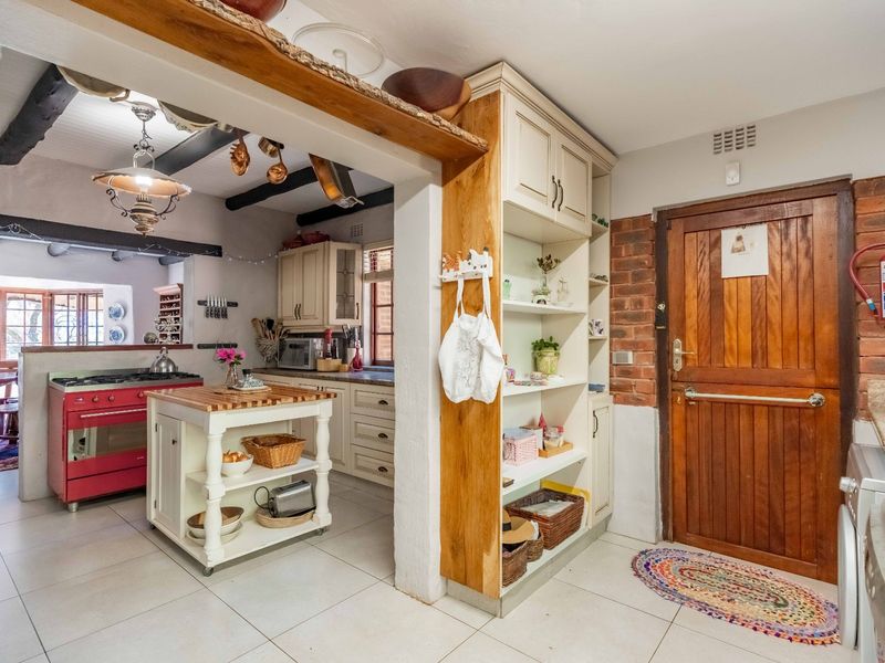 A rustic-style kitchen featuring exposed timber beams, brick accents, built-in cabinetry, and a distinctive red range cooker, creating a warm and characterful cooking space.