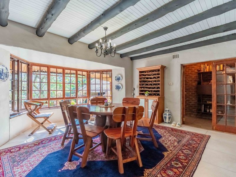 Charming dining room featuring exposed timber ceiling beams, large timber-framed bay windows, and a built-in wine rack, leading into an adjacent room.