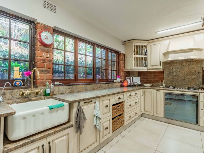 A charming kitchen featuring exposed brick walls, granite countertops, a classic farmhouse sink, and integrated appliances with ample cabinetry.