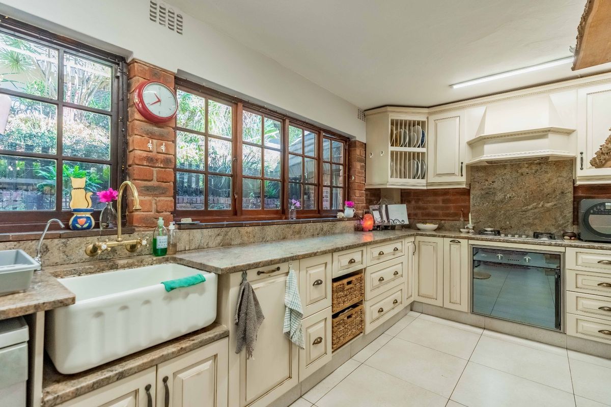 A charming kitchen featuring exposed brick walls, granite countertops, a classic farmhouse sink, and integrated appliances with ample cabinetry.
