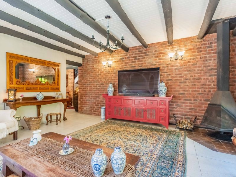 Spacious living room featuring a striking exposed brick wall, a modern freestanding fireplace, and rustic timber ceiling beams, creating a warm and inviting atmosphere.