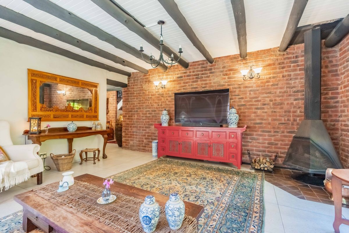 Spacious living room featuring a striking exposed brick wall, a modern freestanding fireplace, and rustic timber ceiling beams, creating a warm and inviting atmosphere.