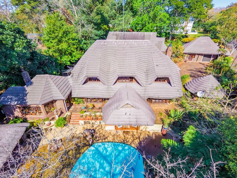 Aerial view of a large residential property featuring a multi-pitched tiled roof, swimming pool, and established garden surroundings.