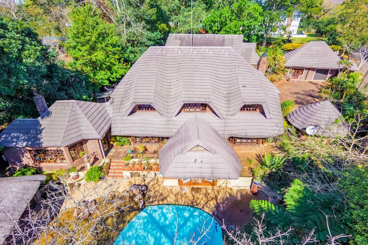 Aerial view of a large residential property featuring a multi-pitched tiled roof, swimming pool, and established garden surroundings.