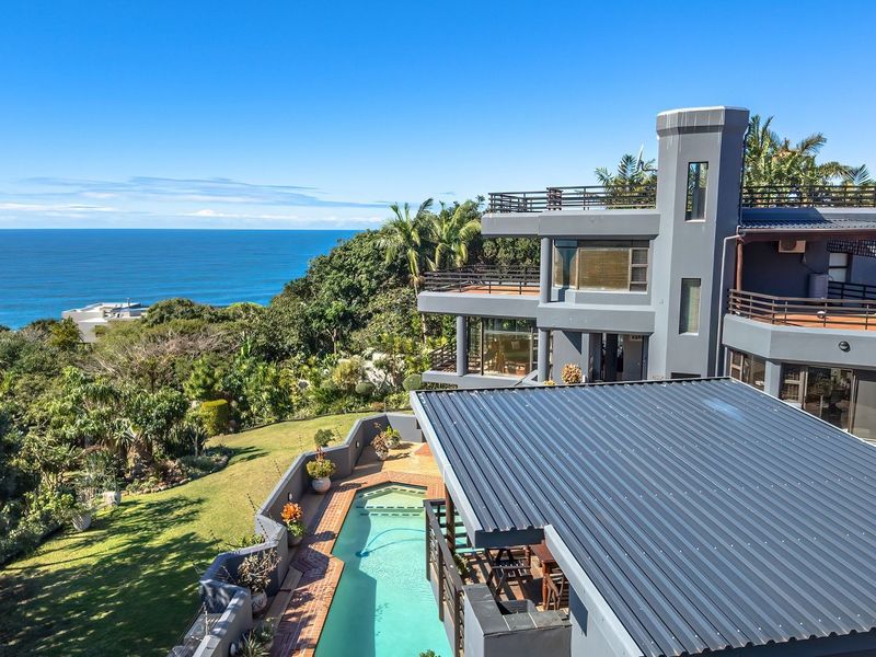 Aerial view of a multi-level coastal residence featuring a swimming pool, expansive balconies, and landscaped gardens overlooking the ocean.