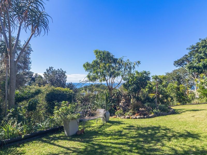 A well-maintained, lush garden featuring mature trees, manicured lawn, and established landscaping with a distant ocean view.
